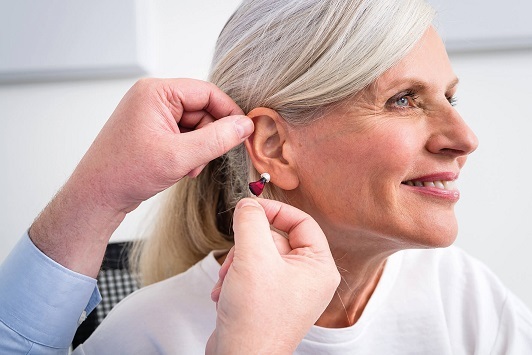 Ältere Frau bekommt ein modernes Hörgerät ins Ohr eingesetzt, Hörakustiker Beratung.